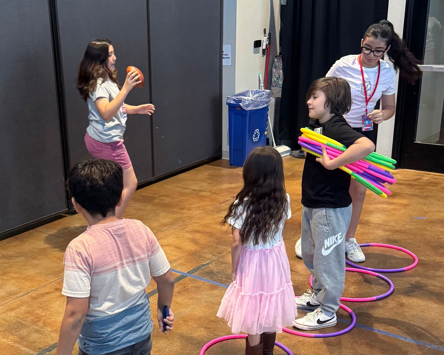 Children playing with hula hoops on a polished wooden floor in an indoor setting.